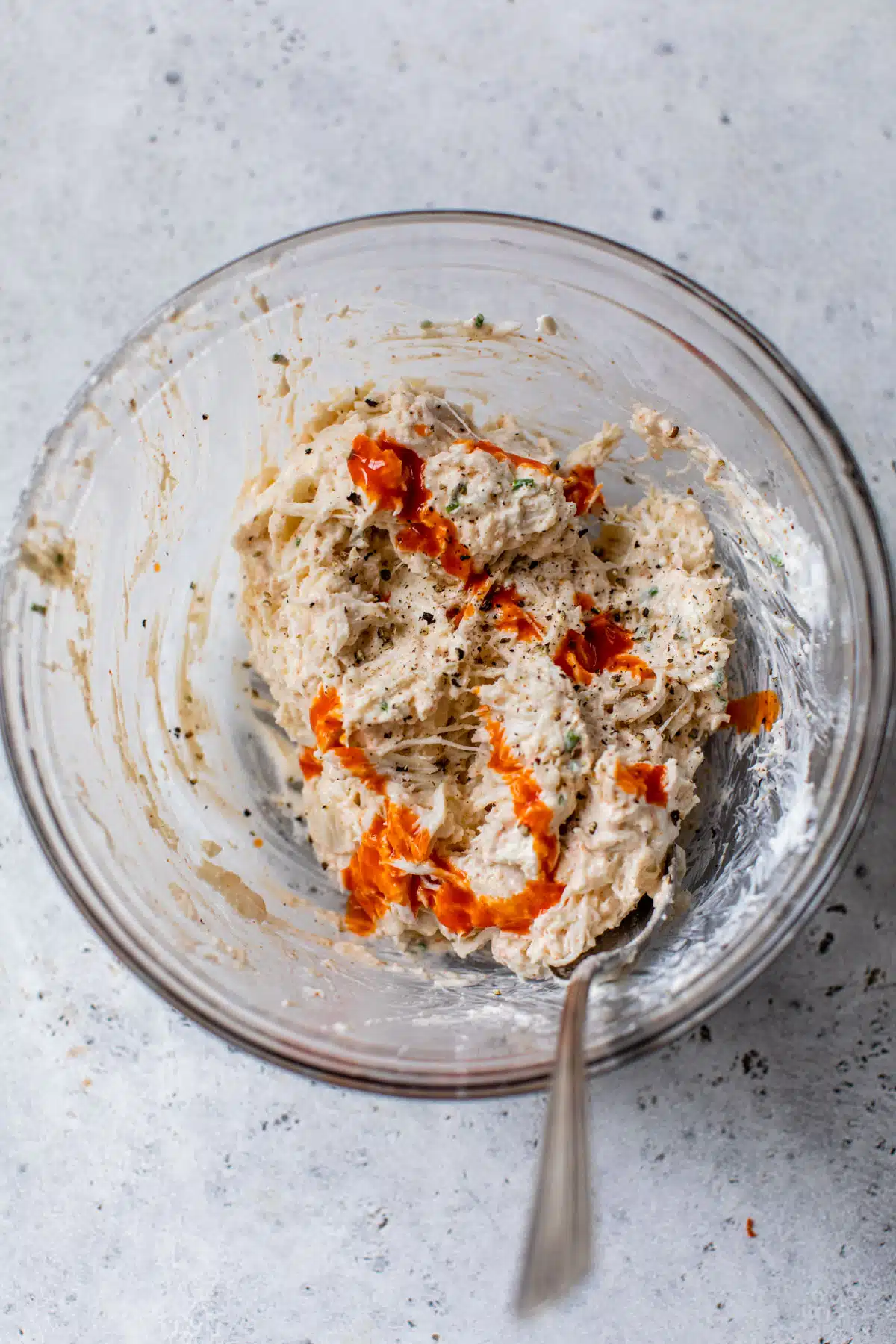 crab dip mixture with hot sauce added in a glass bowl with a spoon