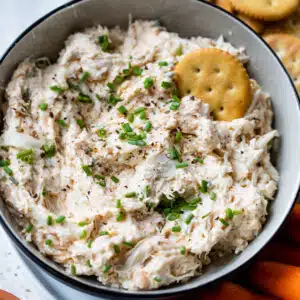 cold crab dip in a bowl with chives and a cracker on top and on a plate with crackers and carrots