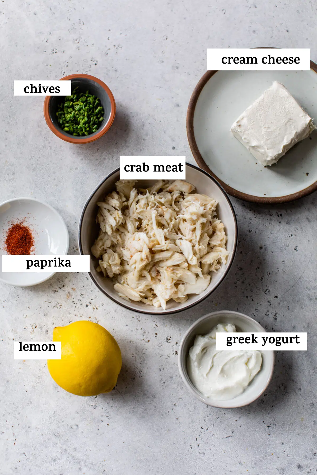 all ingredients on a table; chives, cream cheese, paprika, crab meat, lemon, and greek yogurt