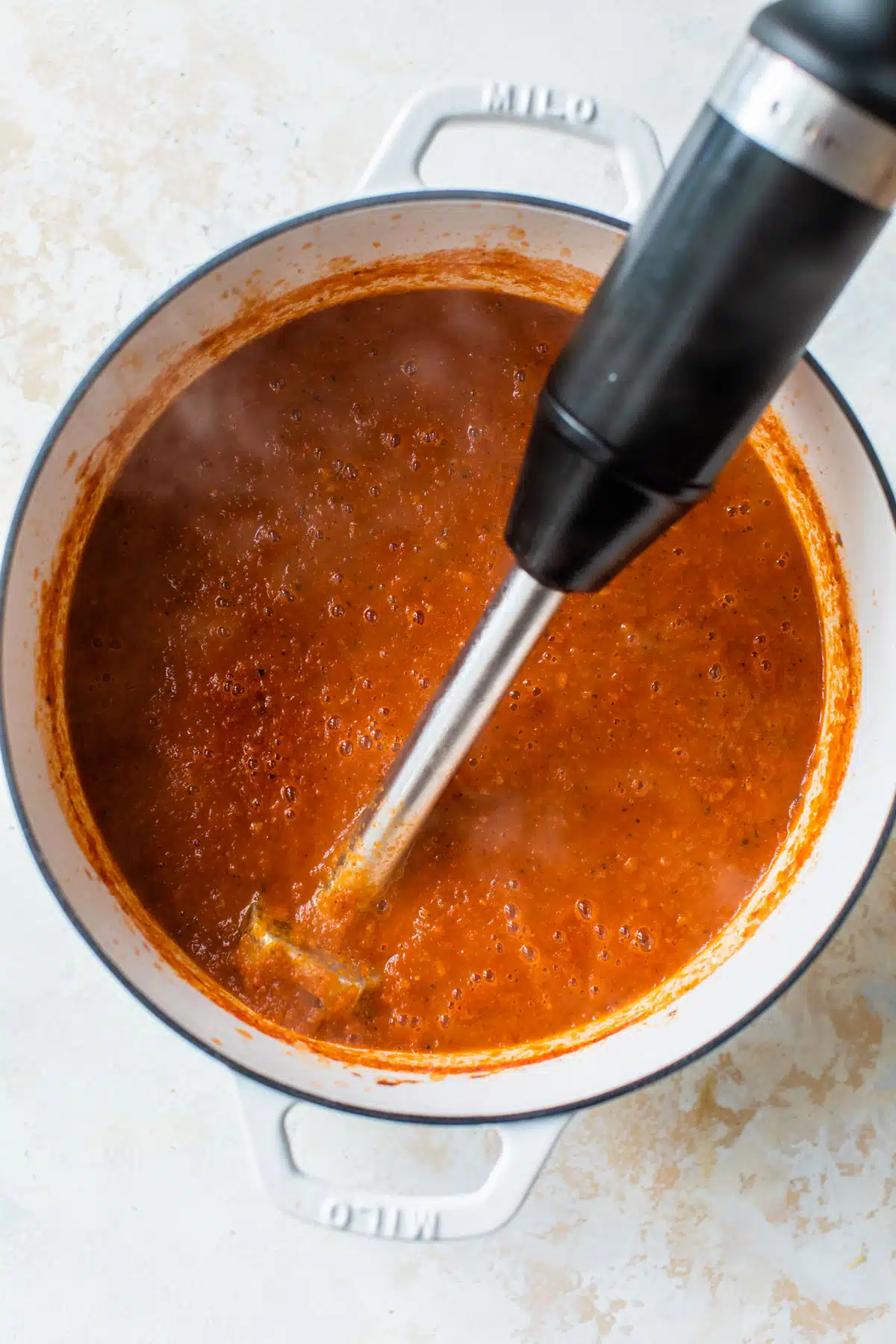 creamy tomato basil soup being blended by an immersion blender in a dutch oven