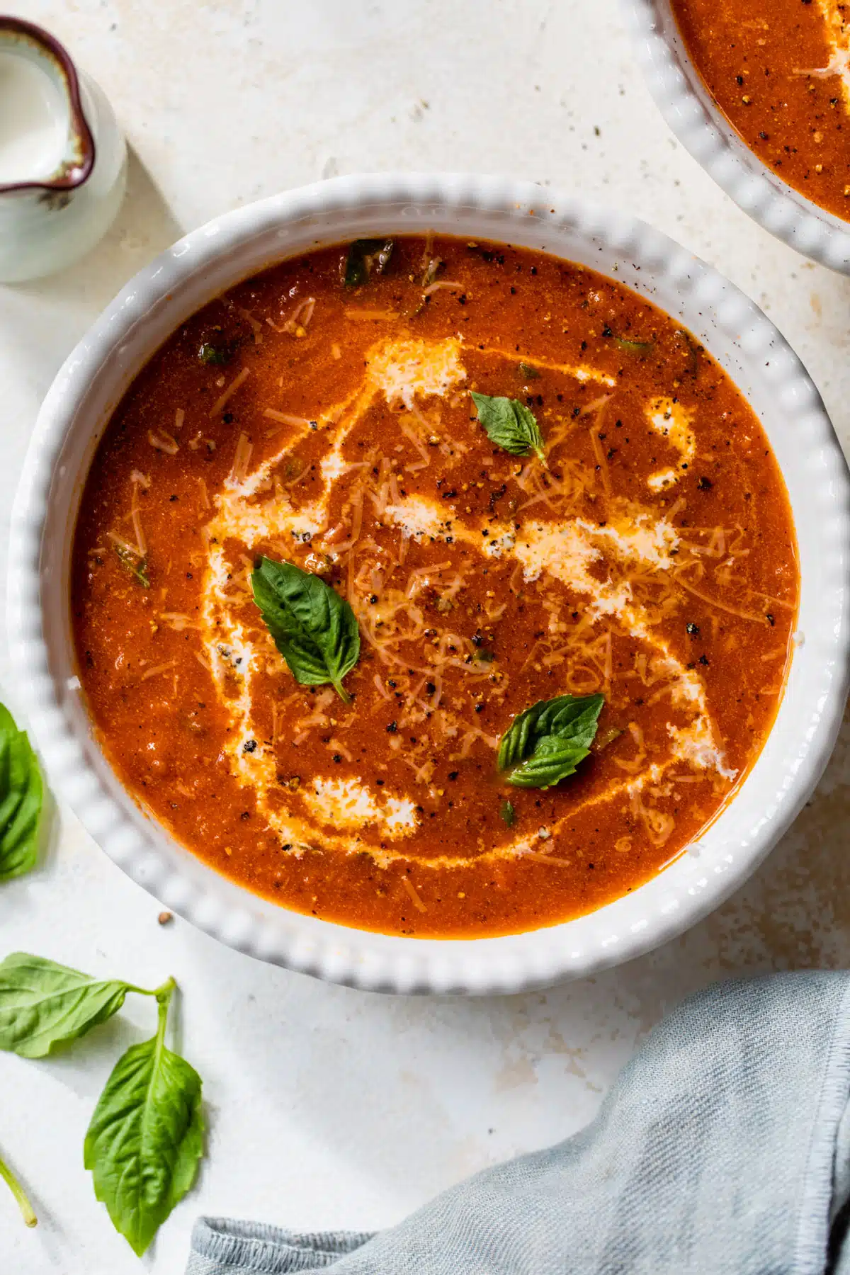 creamy tomato basil soup in a bowl with half & half drizzled in and basil leaves on top
