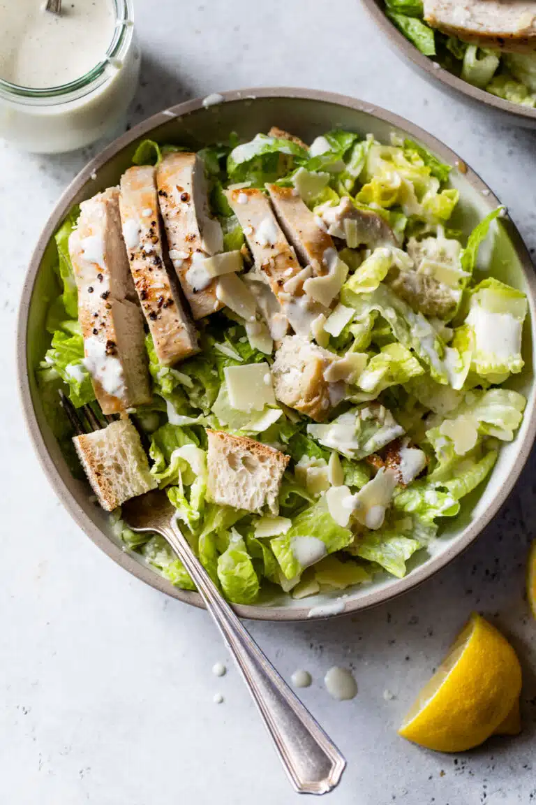 grilled chicken caesar salad in a bowl with dressing on top and a fork