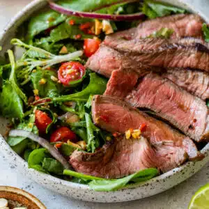 side view of Thai steak salad in a bowl topped with sliced sirloin steak