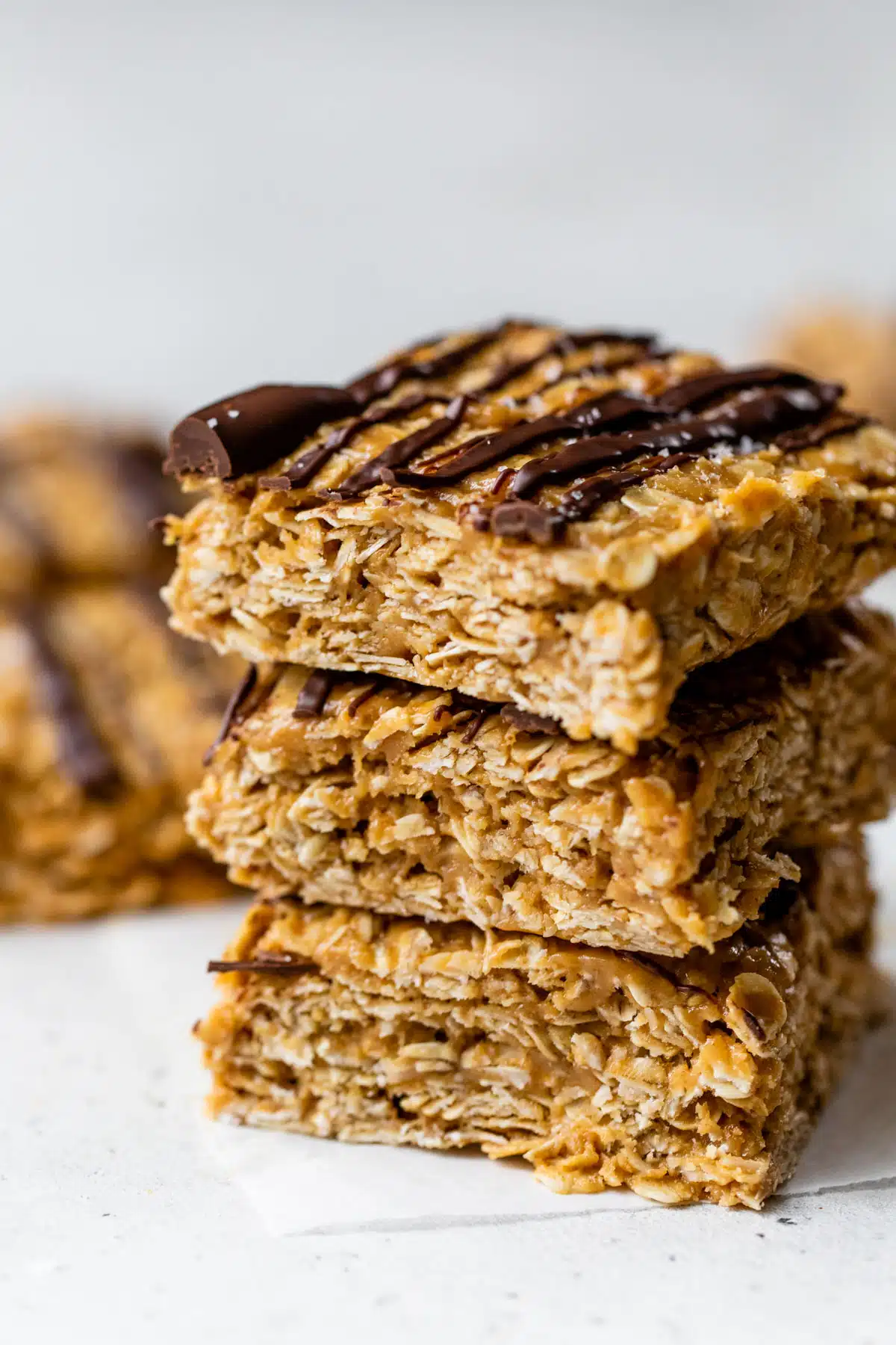 side view of three peanut butter oatmeal bars with melted chocolate drizzled over top stacked on top of each other