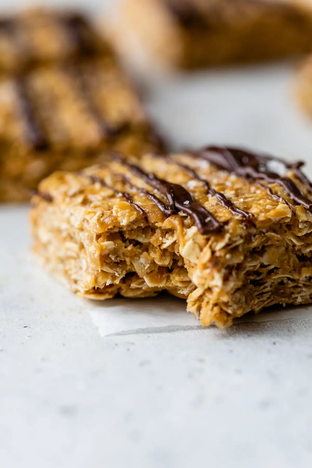 side view of a peanut butter oatmeal bar with melted chocolate drizzled over top with a bite taken out