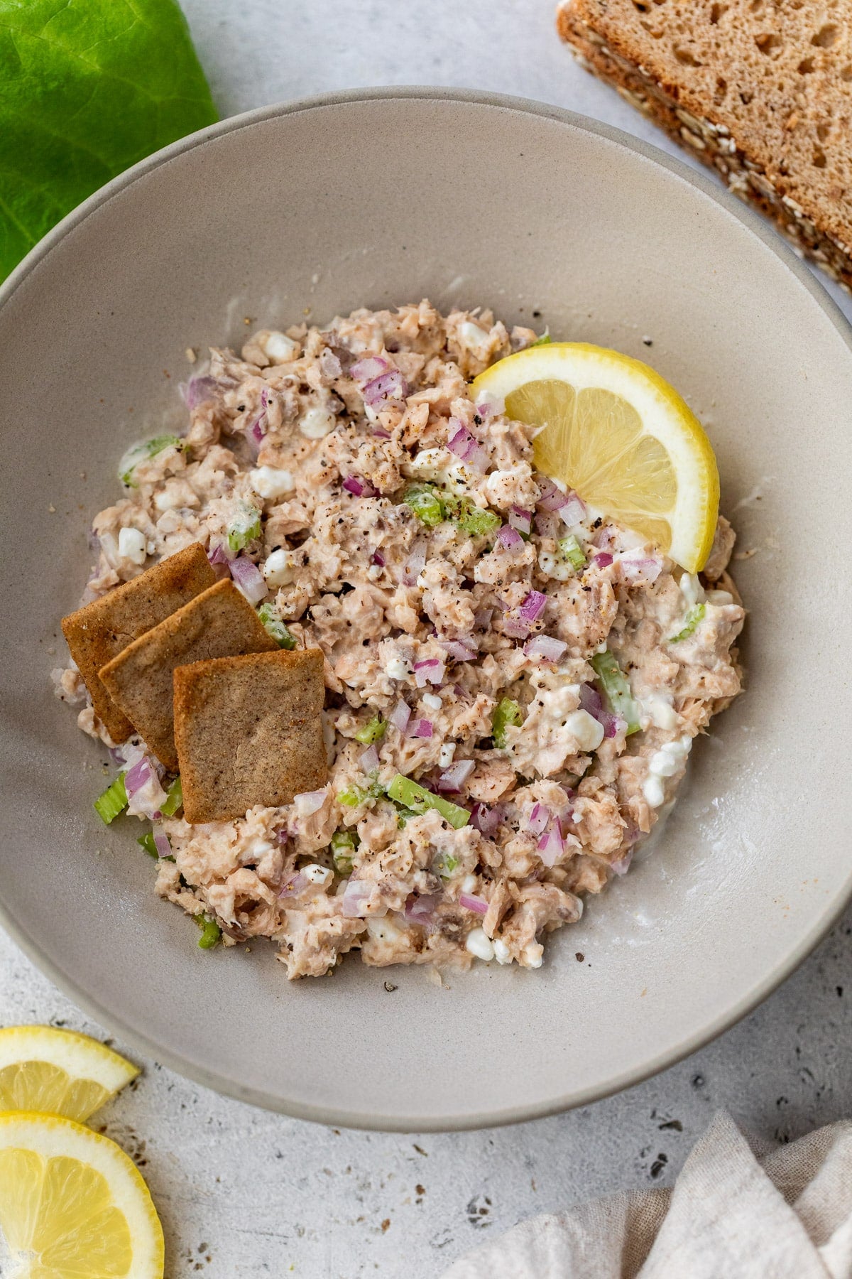 a bowl of salmon salad topped with a lemon wedges and crackers.