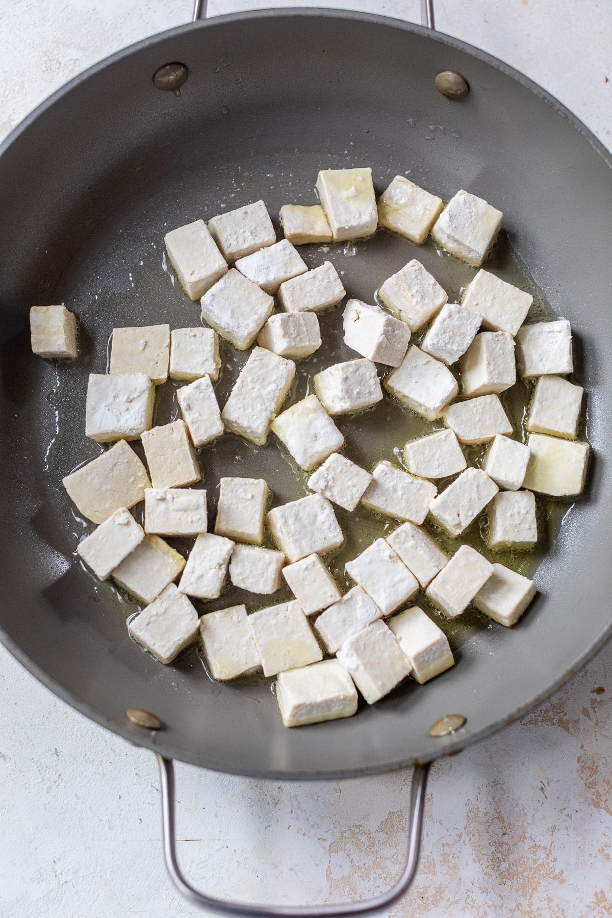 frying cornstarch-coated tofu cubes in a large grey skillet.