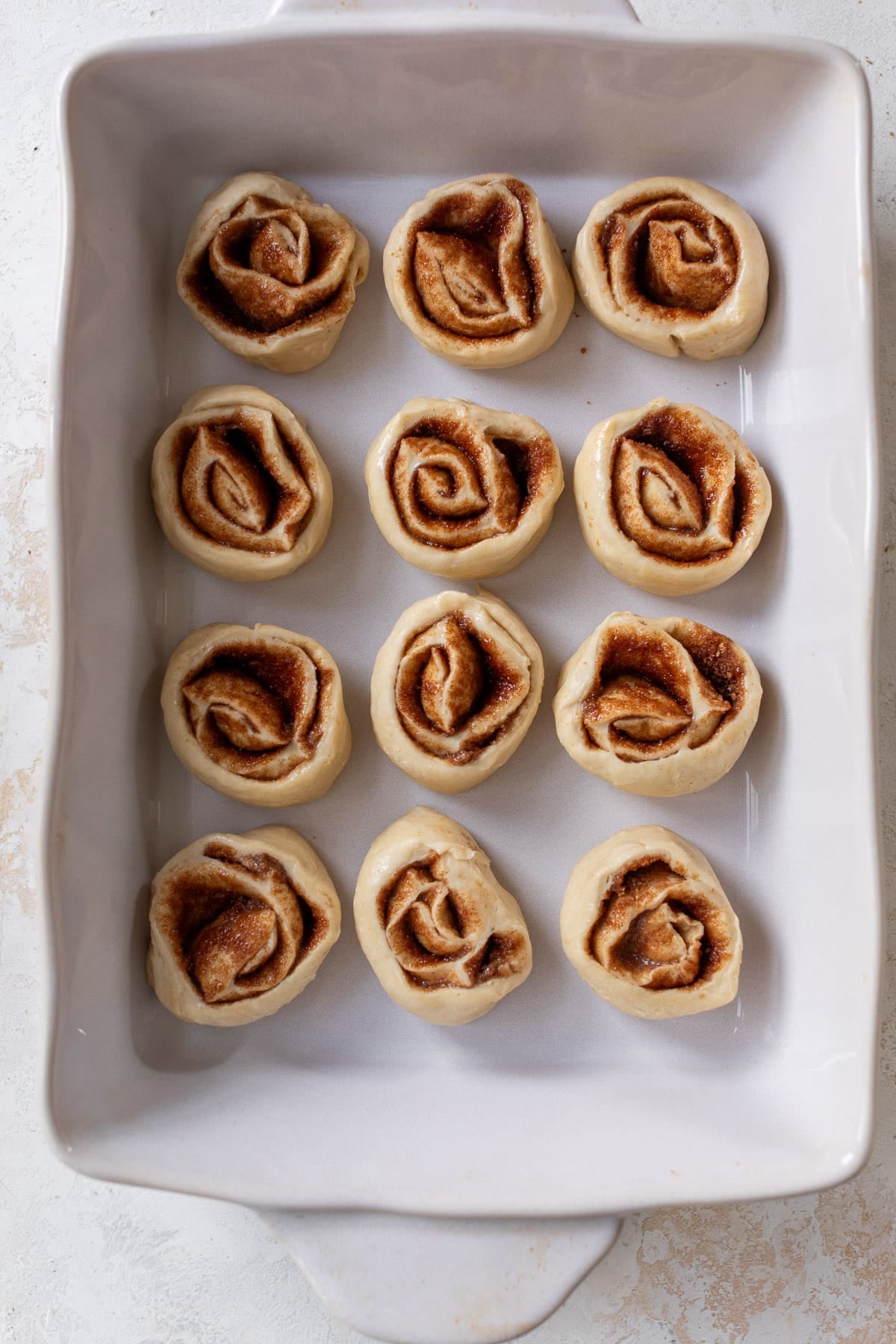 overhead view of unbaked vegan cinnamon rolls in a white baking dish.