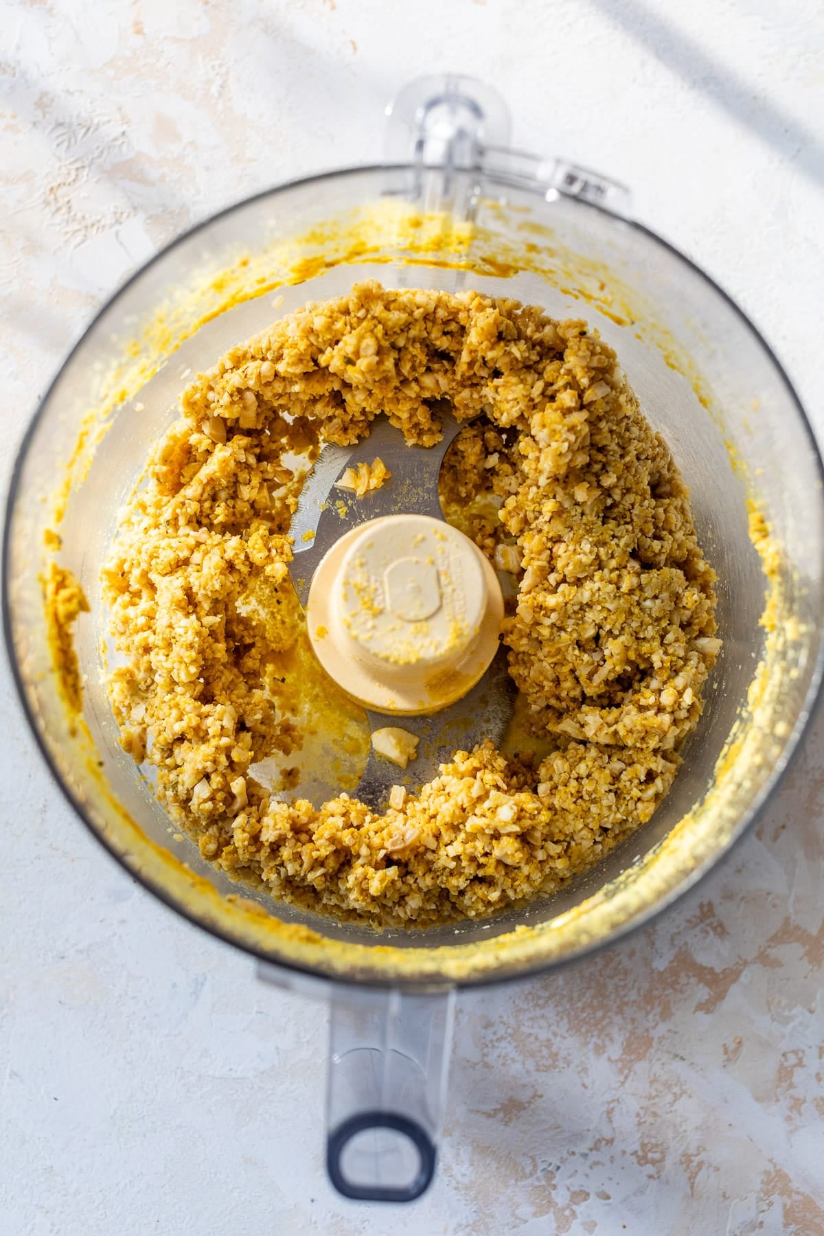 overhead view of a crumbly vegan ricotta cheese for vegan lasagna in a food processor.