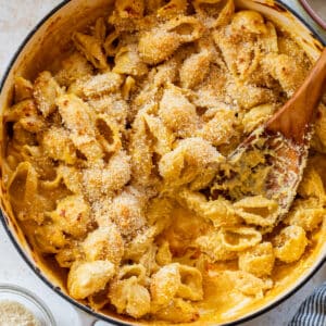 overhead view of a wooden spoon scooping vegan mac and cheese from a large pot.
