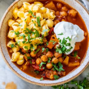 overhead view of a bowl of Butternut Squash Chickpea Chili topped with mac and cheese and sour cream.