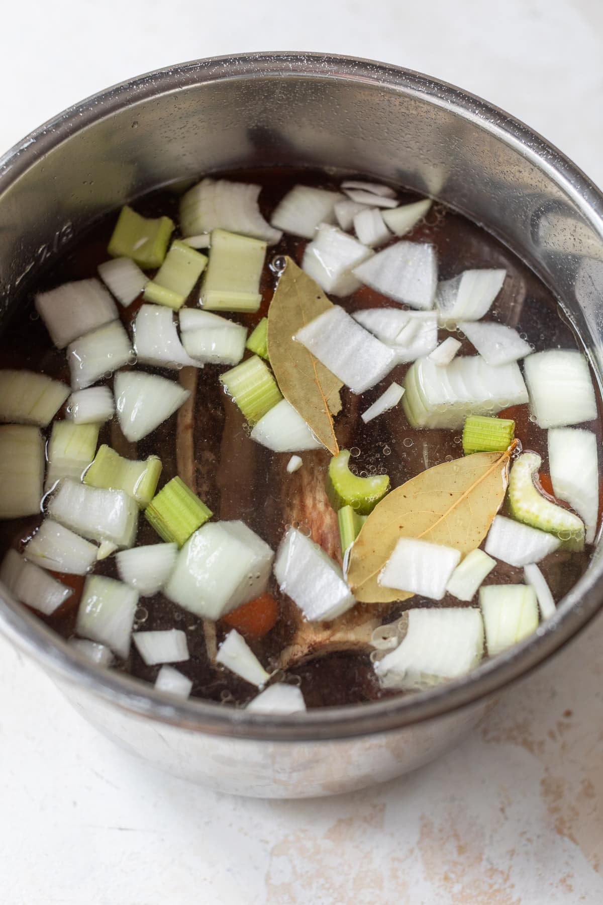 overhead view of water and the ingredients for bone broth in an instant pot.
