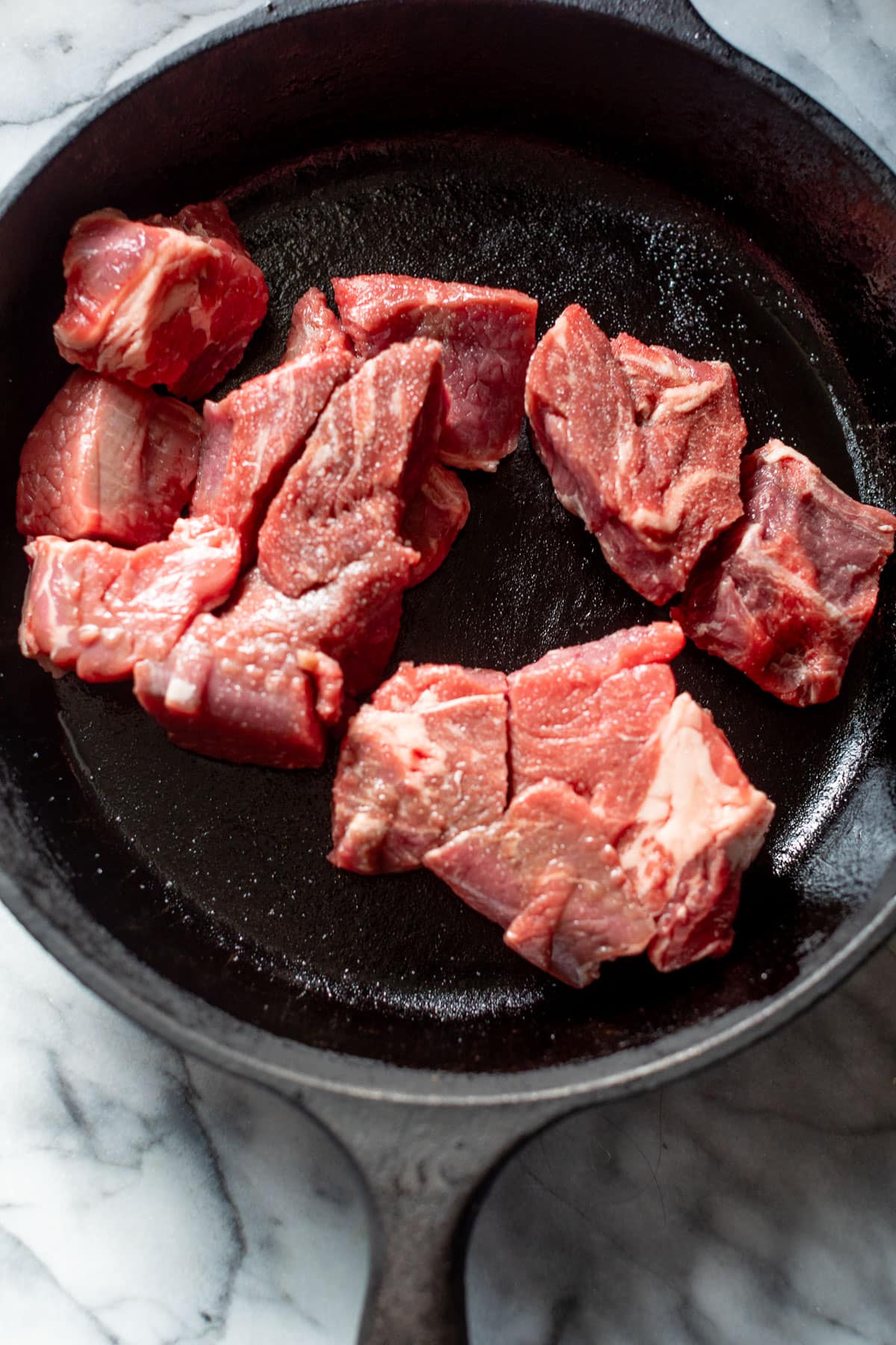 overhead view of raw beef pieces in a black skillet.