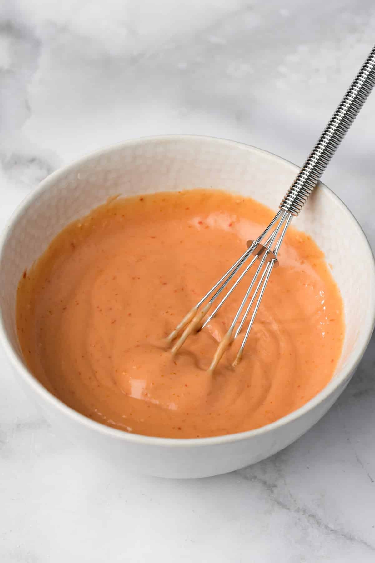 a whisk in a bowl of bang bang sauce.