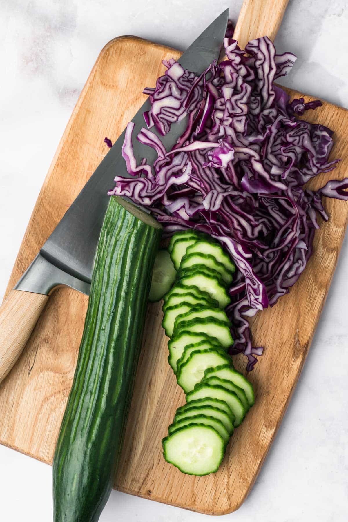 sliced cucumbers and red cabbage on a cutting board.
