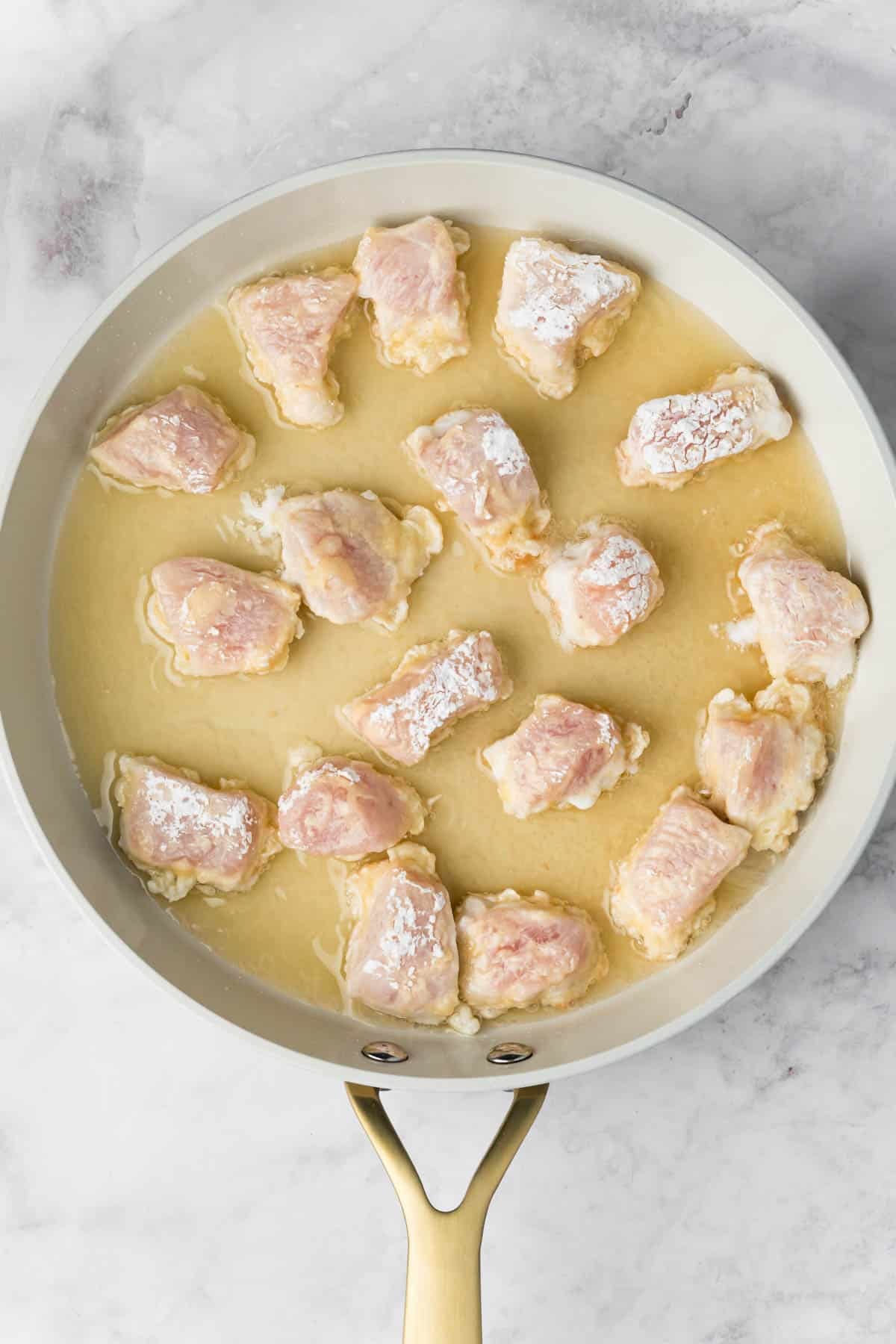 overhead view of raw chicken pieces frying in a skillet.