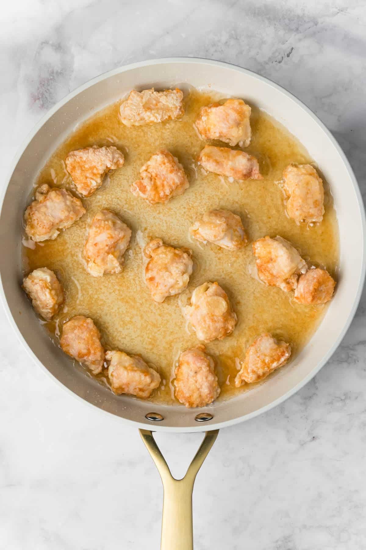 overhead view of chicken pieces frying in a skillet.