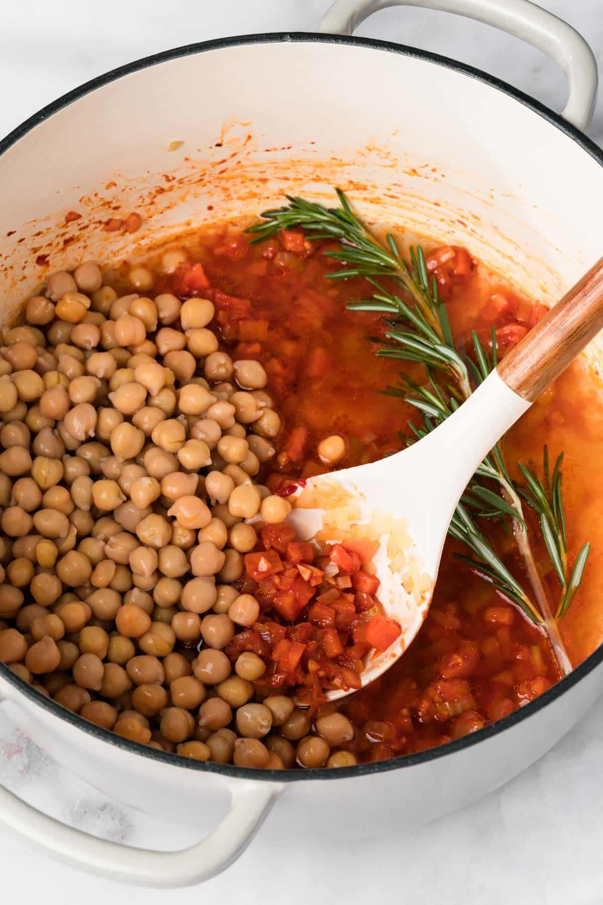 overhead view of a white spoon stirring chickpeas into a pot for pasta e ceci.