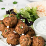 side view on a pile of spicy lamb meatballs on a plate with greens and pita.