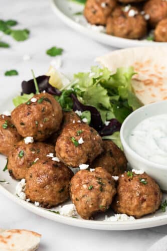 side view on a pile of spicy lamb meatballs on a plate with greens and pita.