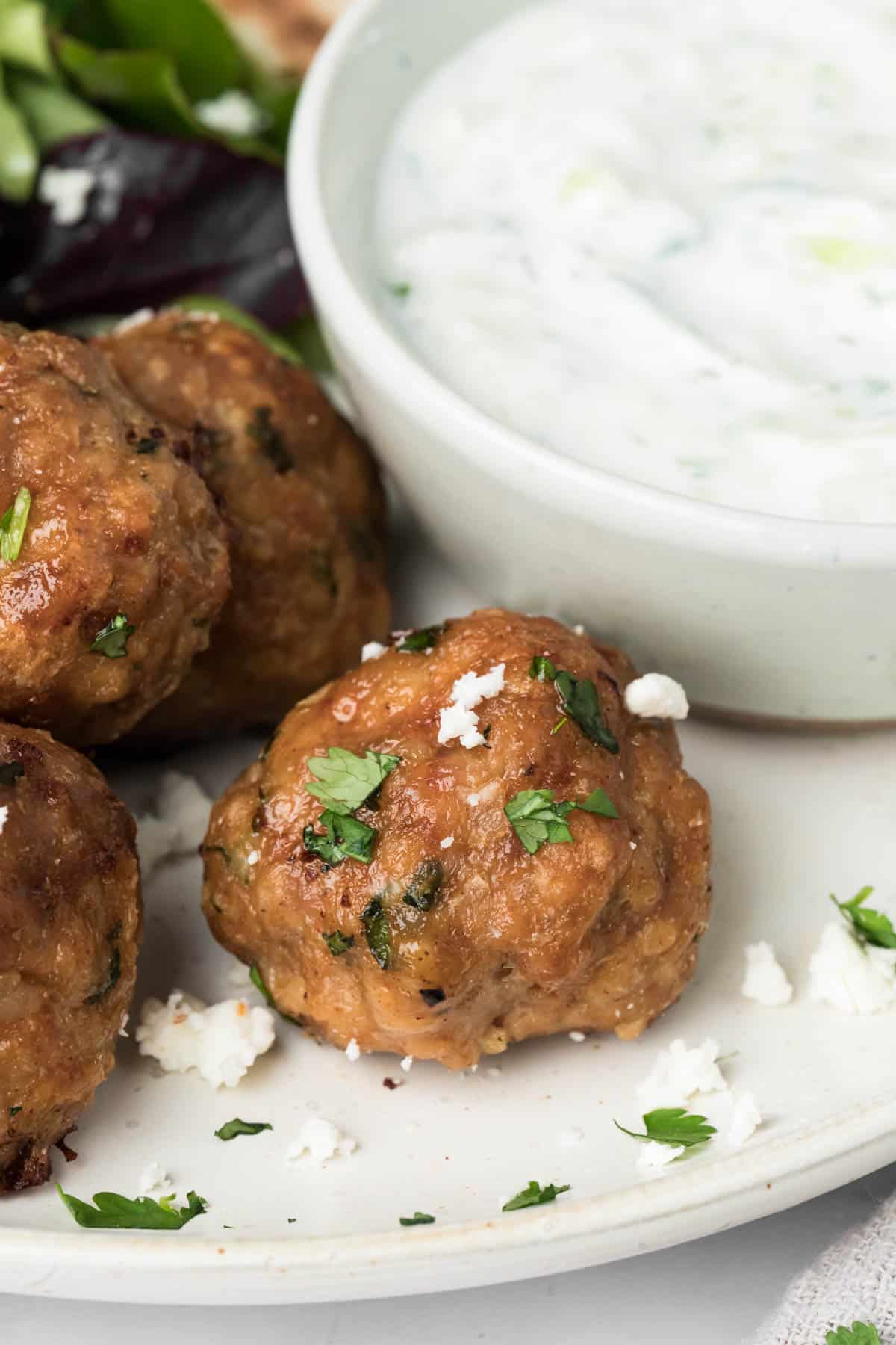 close up on a spicy lamb meatball next to a small bowl of tzatziki.