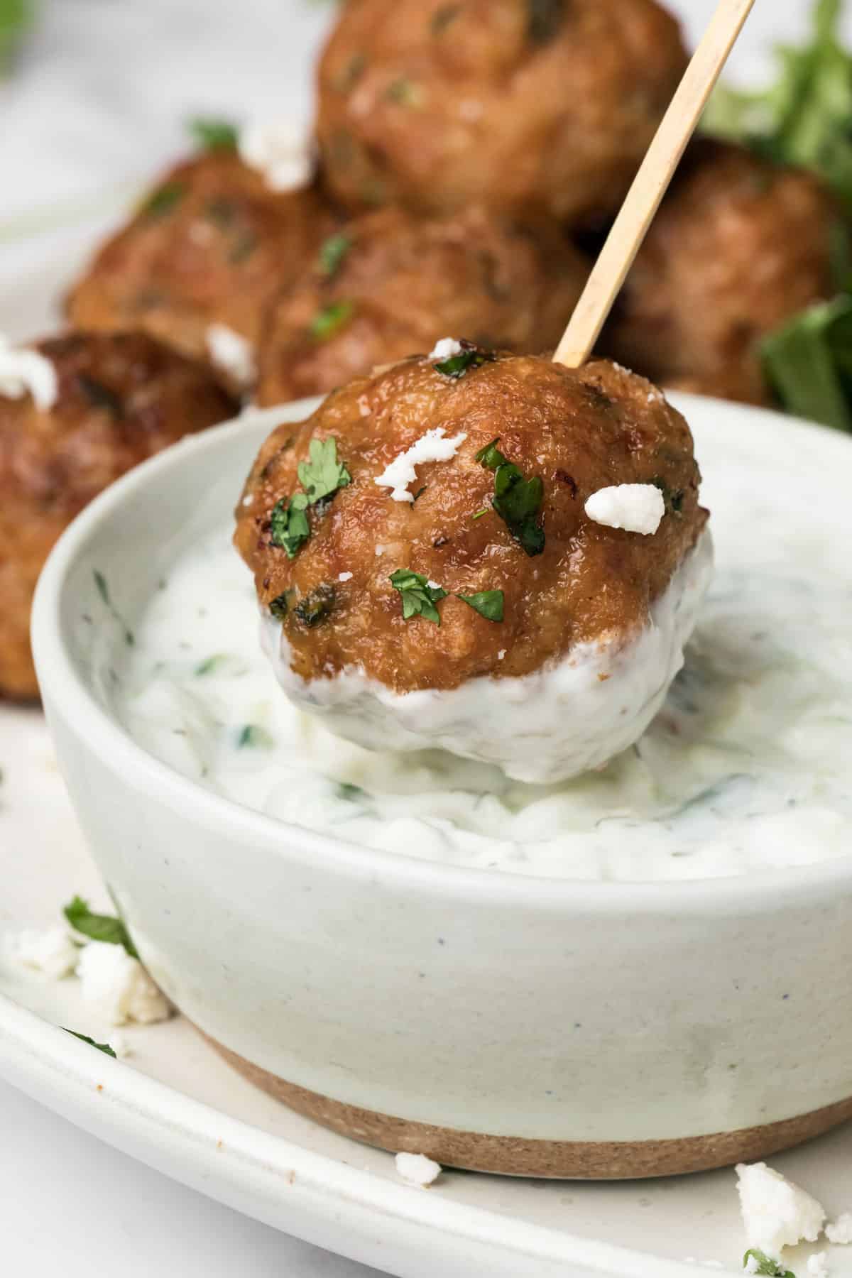 close up on a spicy lamb meatball being dipped into a small bowl of tzatziki.