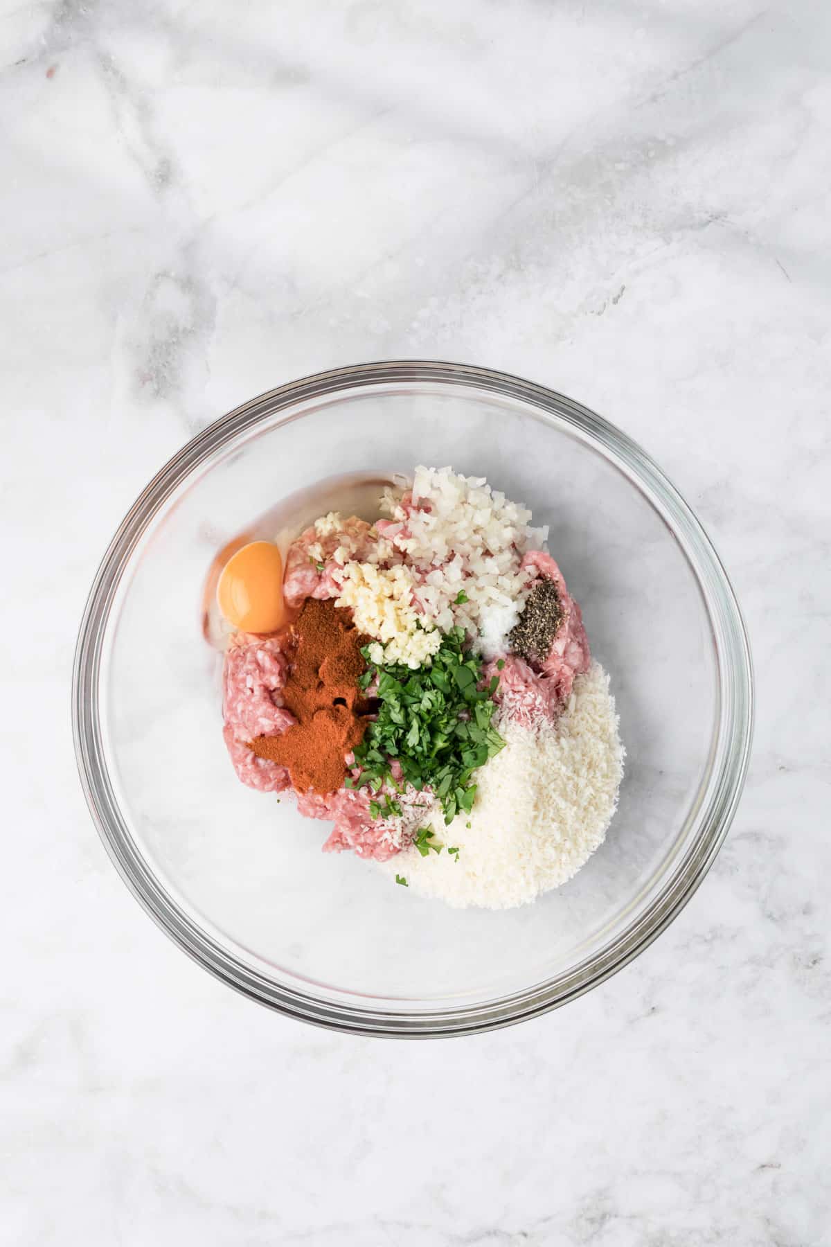 overhead view of the ingredients for spicy lamb meatballs in a glass bowl.