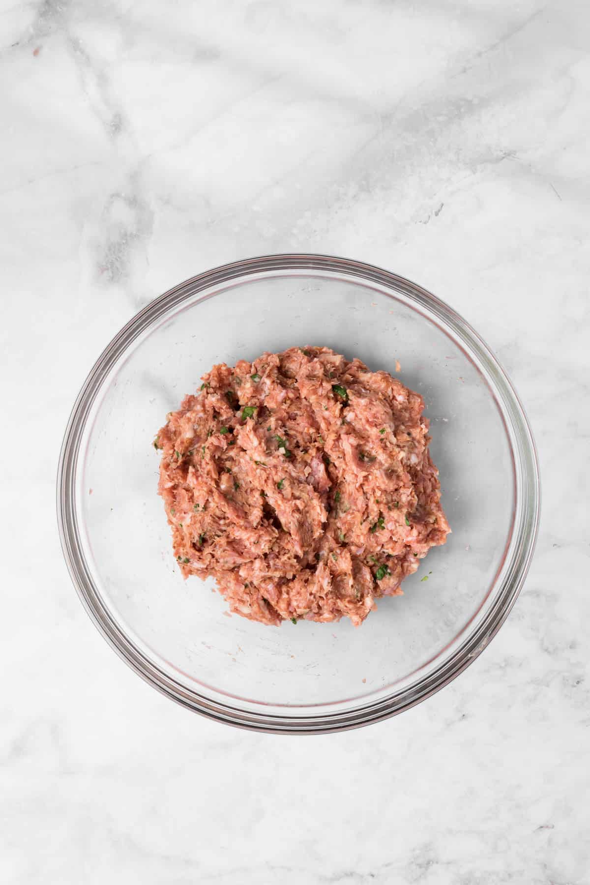 overhead view of a raw spicy lamb meatball mixture in a glass bowl.