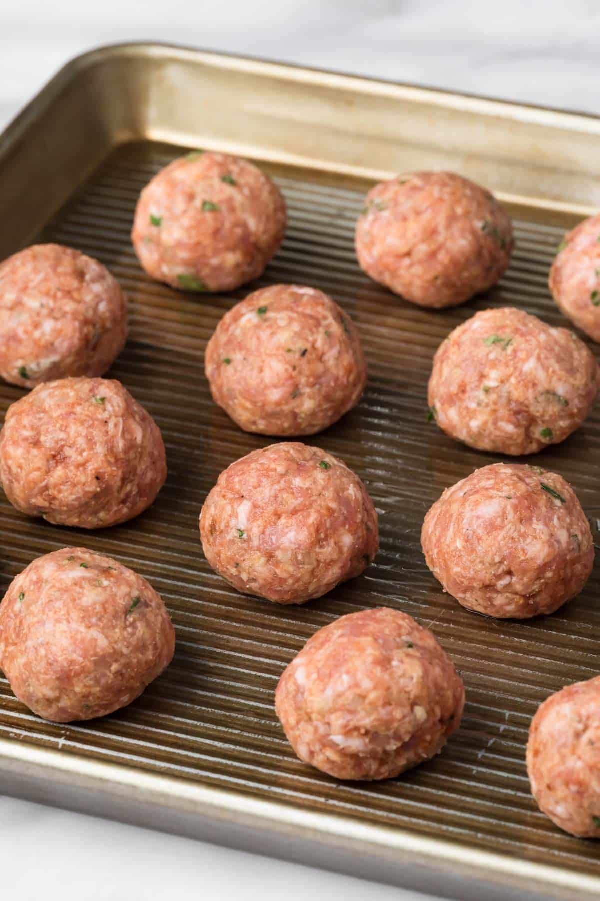 side view of raw spicy lamb meatballs on a baking sheet.