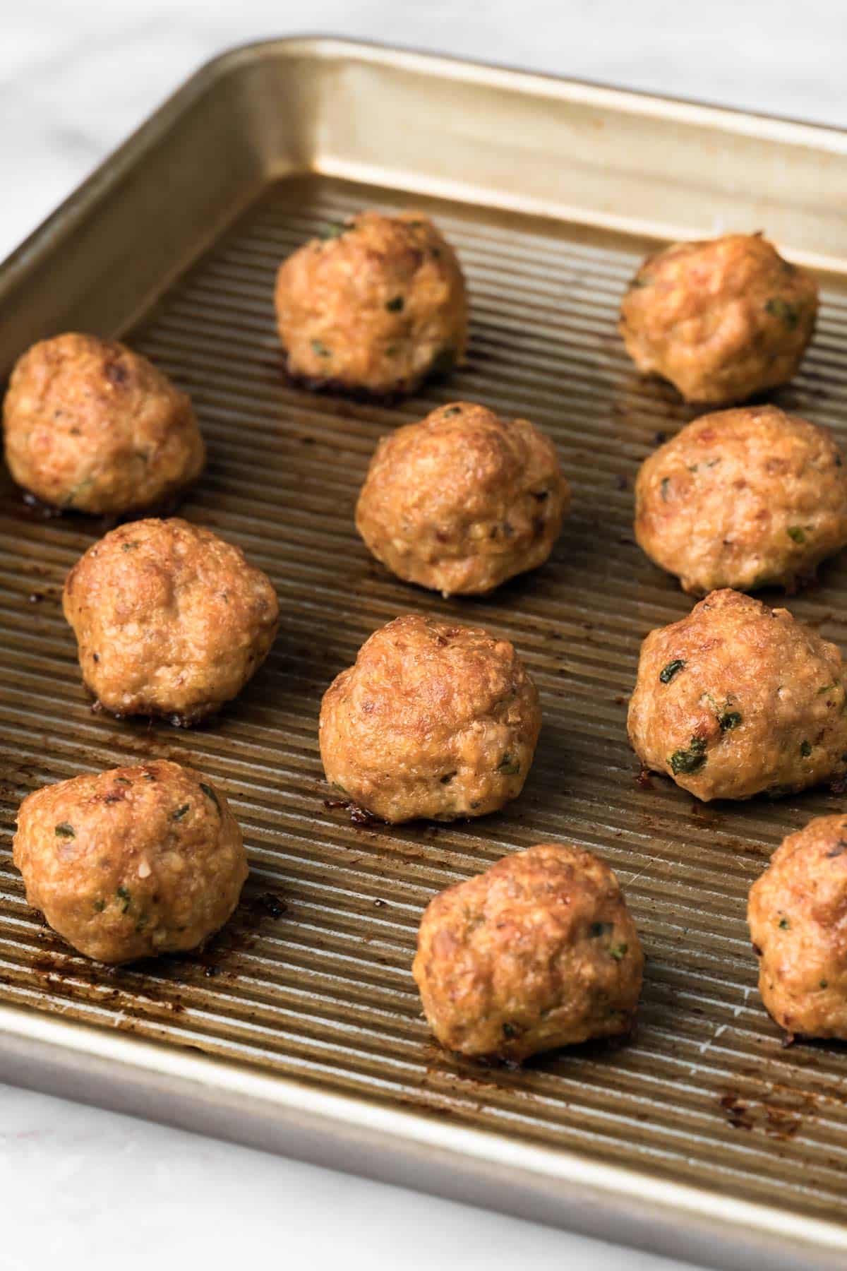 side view of baked spicy lamb meatballs on a baking sheet.