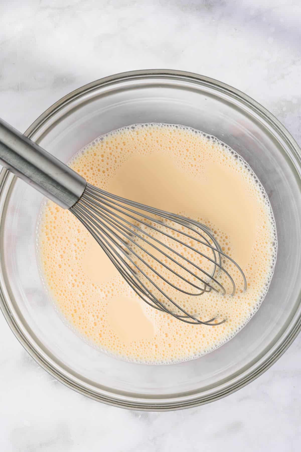 overhead view of a liquid mixture for chia seed pancake batter and a whisk in a large glass bowl.