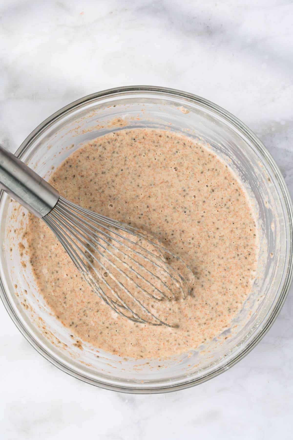 overhead view of chia seed pancake batter and a whisk in a large glass bowl.