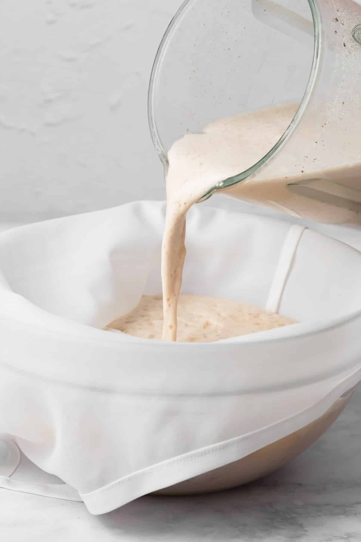 pouring blended horchata through a nut milk bag into a large bowl.
