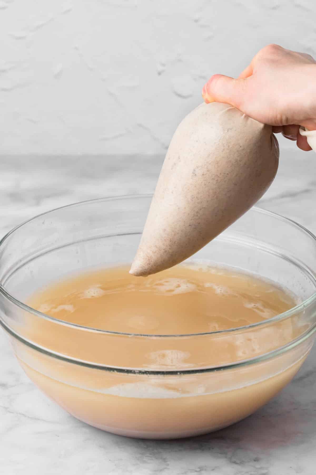 straining blended horchata from a nut milk bag into a large glass bowl.