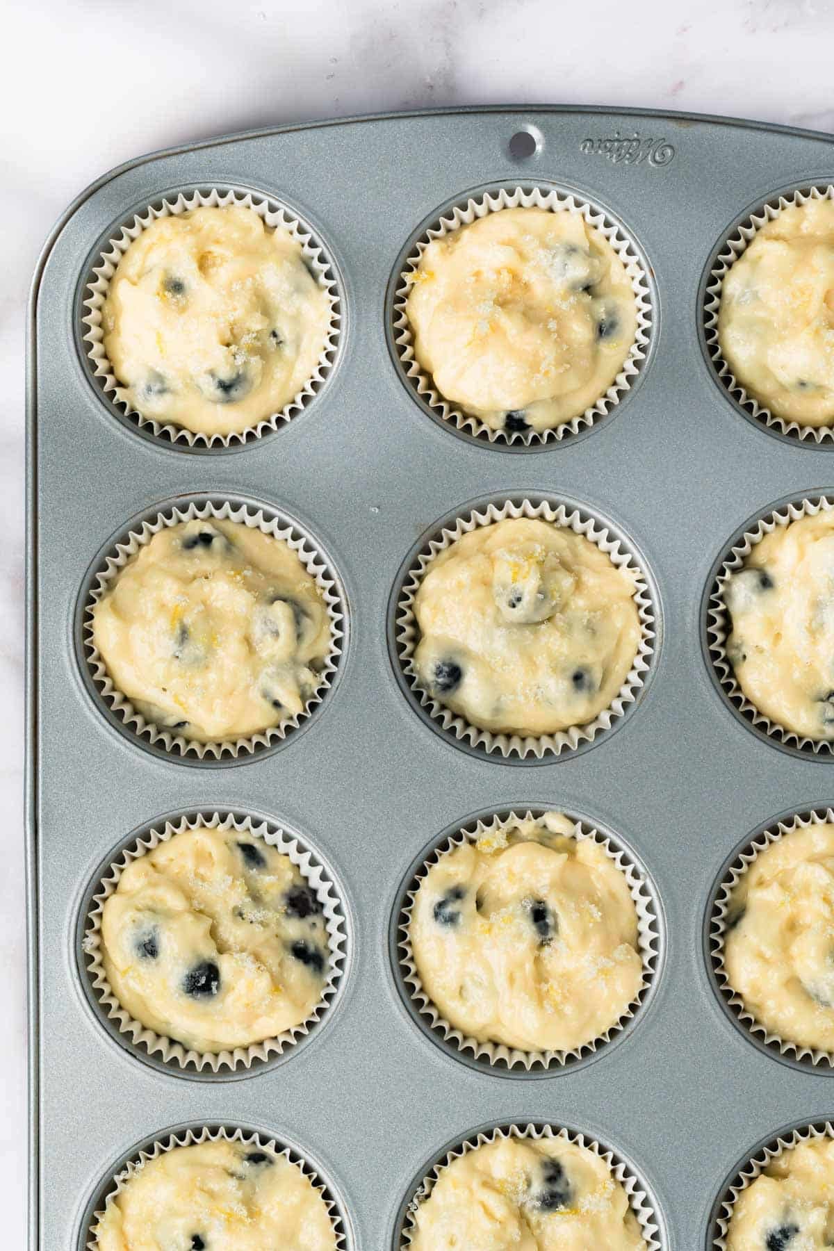 overhead view of unbaked lemon blueberry muffins in a muffin tin.
