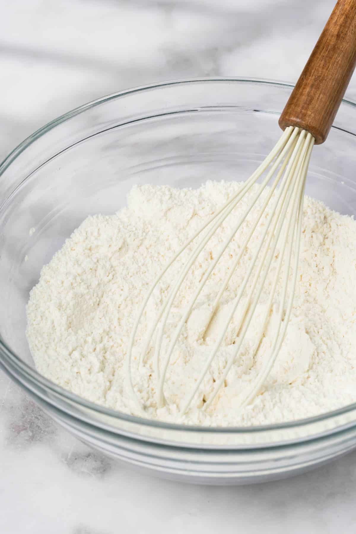 close up on the dry ingredients for lemon blueberry muffins and a white whisk in a bowl.