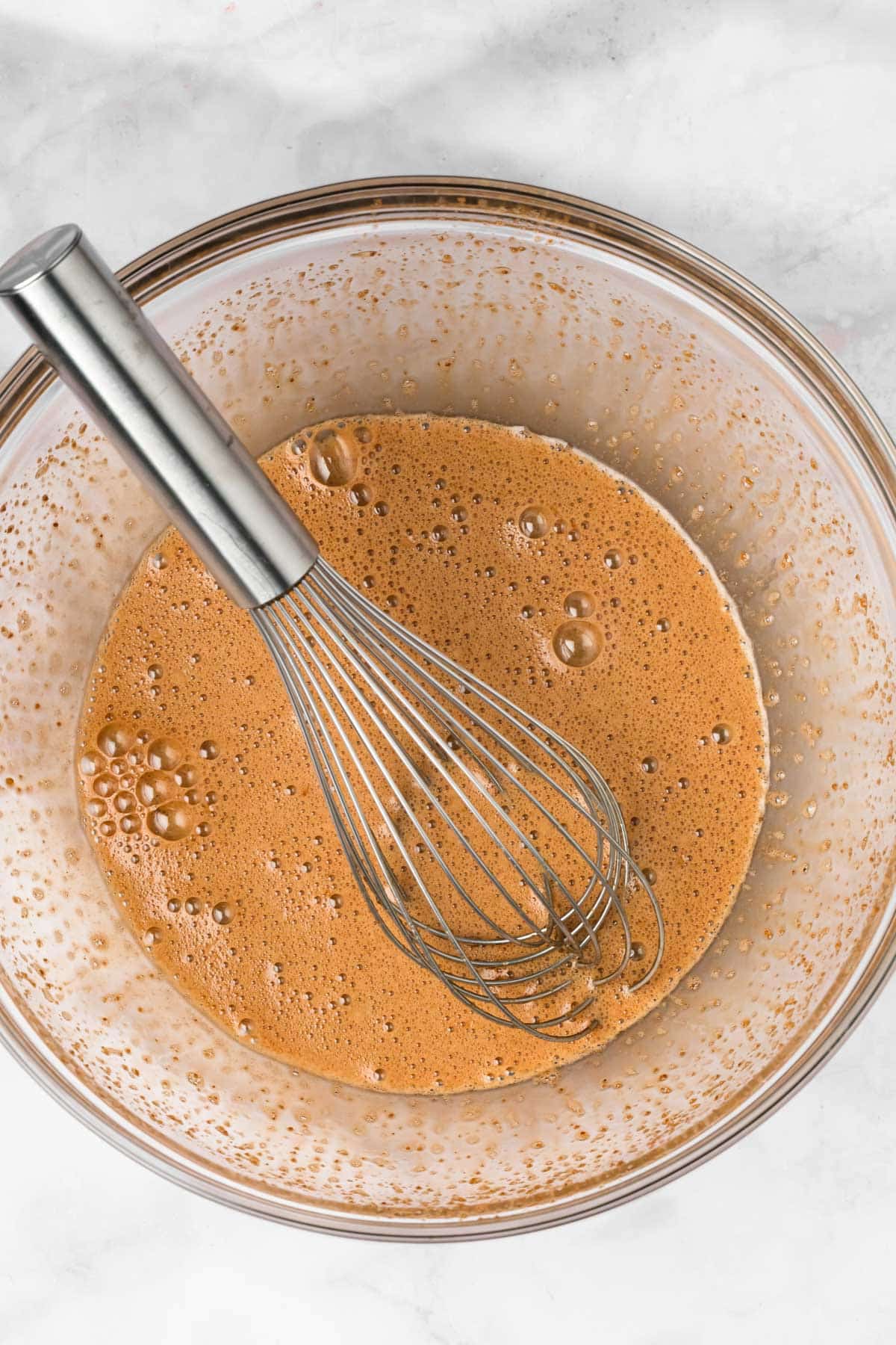 overhead view of a whisk in a bowl with the liquid mixture for paleo brownies.