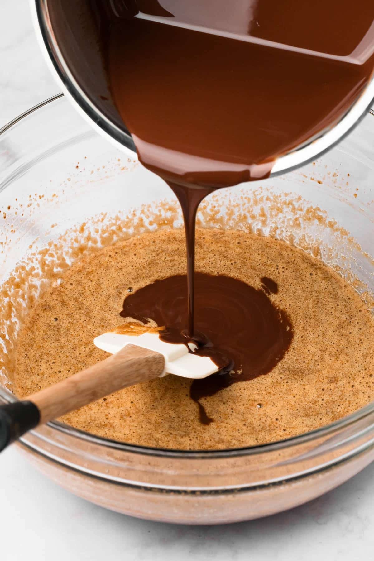 pouring melted chocolate into the liquid ingredient mixture for paleo brownies.