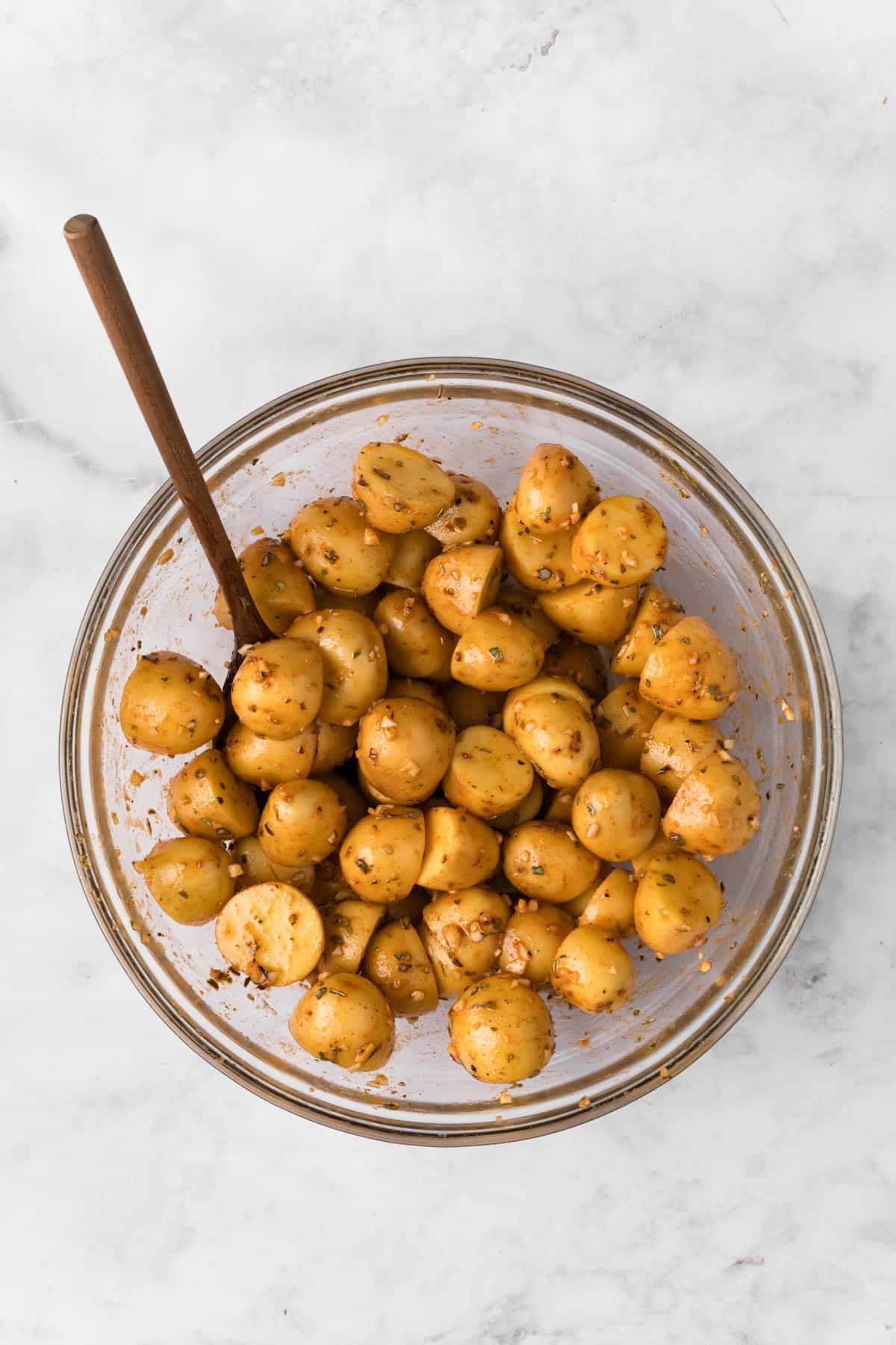 Overhead view of seasoned raw baby potatoes in a glass bowl.