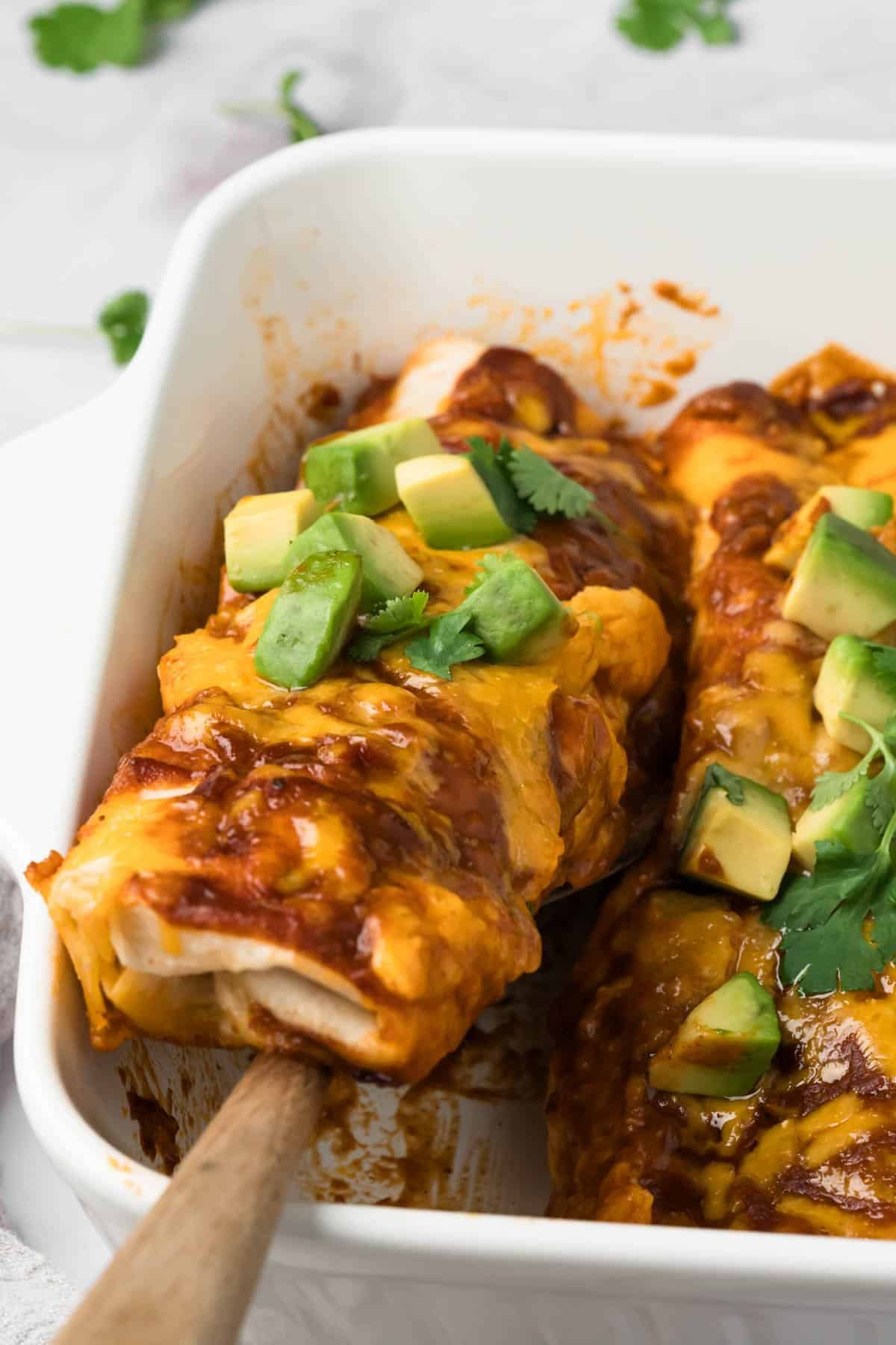 close up on a tofu enchilada being lifted out of a baking dish.