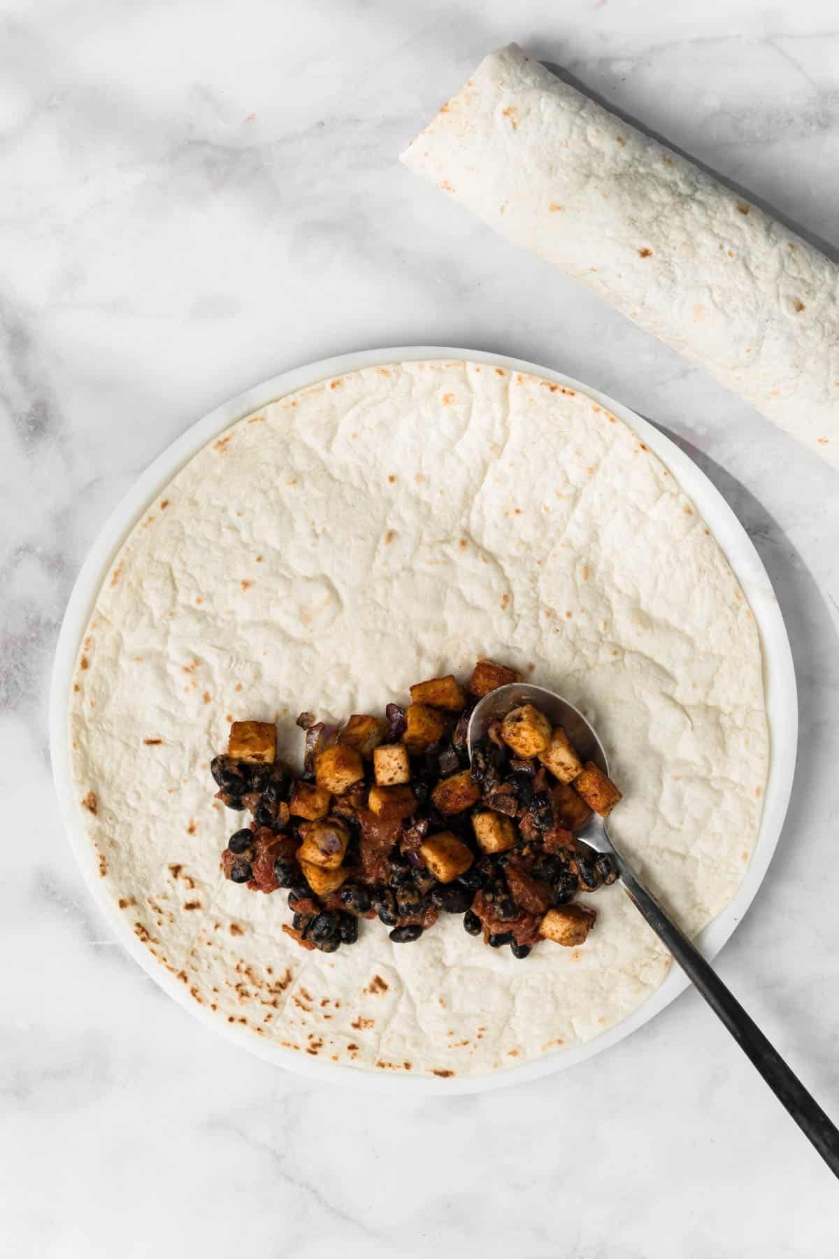 overhead view of the tofu enchilada filling being spooned into a tortilla.