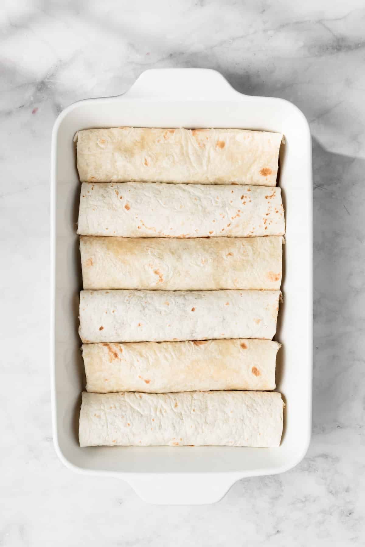 overhead view of unbaked rolled tofu enchiladas in a baking dish.