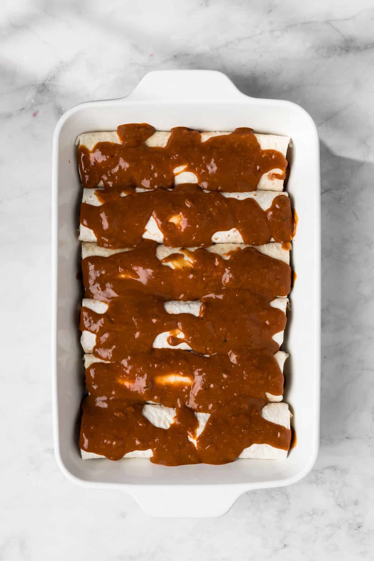 overhead view of unbaked tofu enchiladas topped with enchilada sauce in a baking dish.
