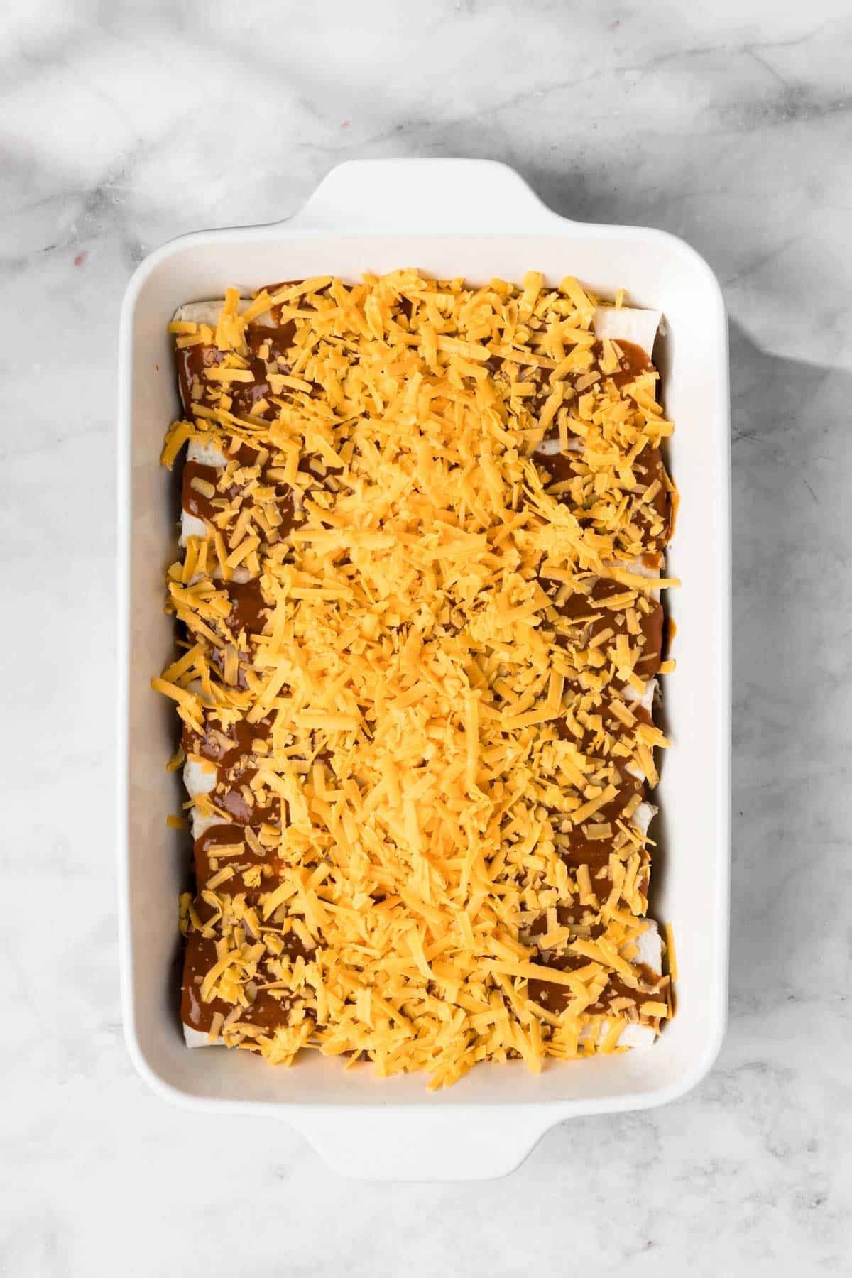 overhead view of unbaked tofu enchiladas topped with vegan cheese in a baking dish.
