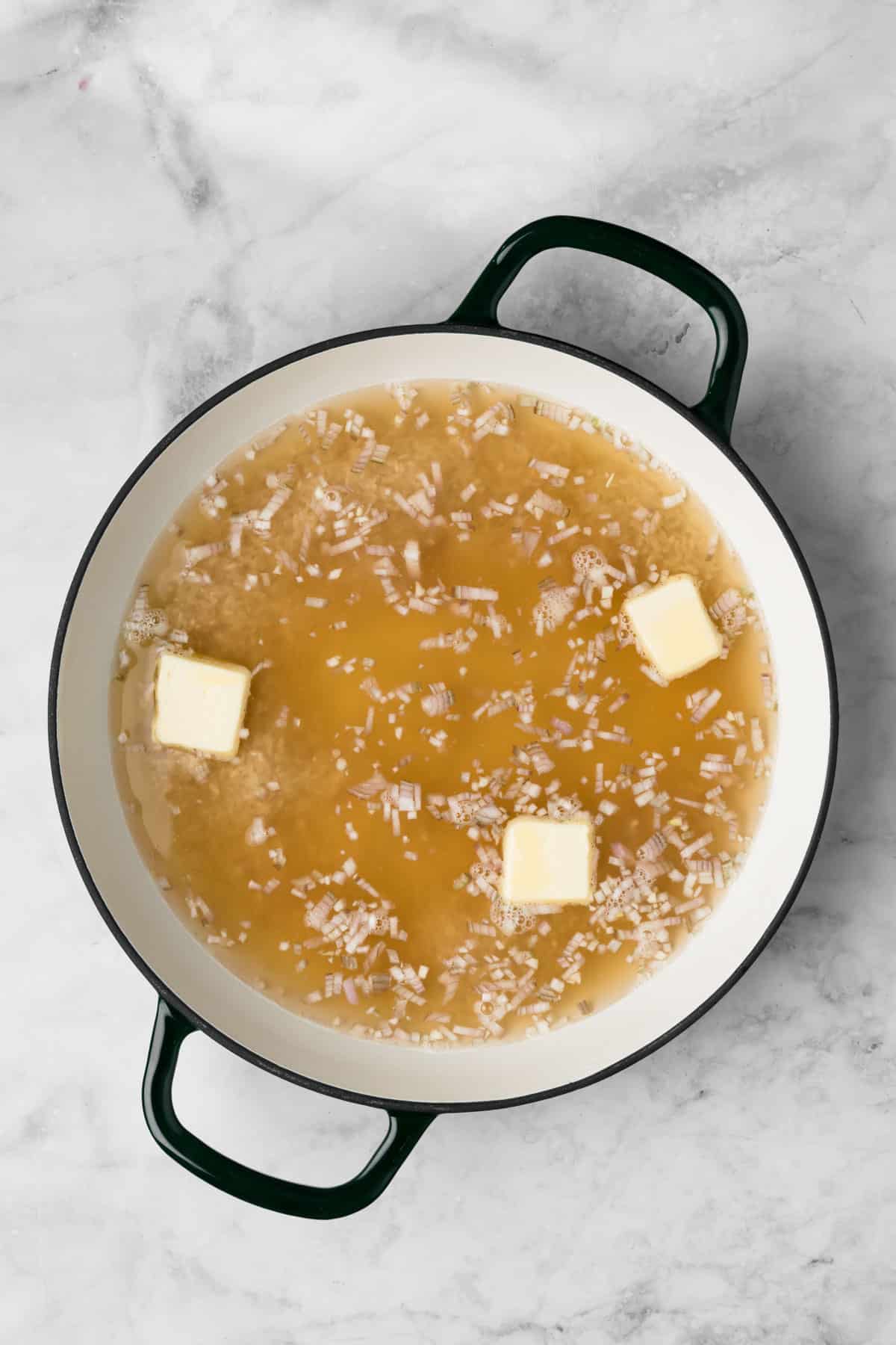 overhead view of broth, shallots, and butter in a pot for baked risotto.