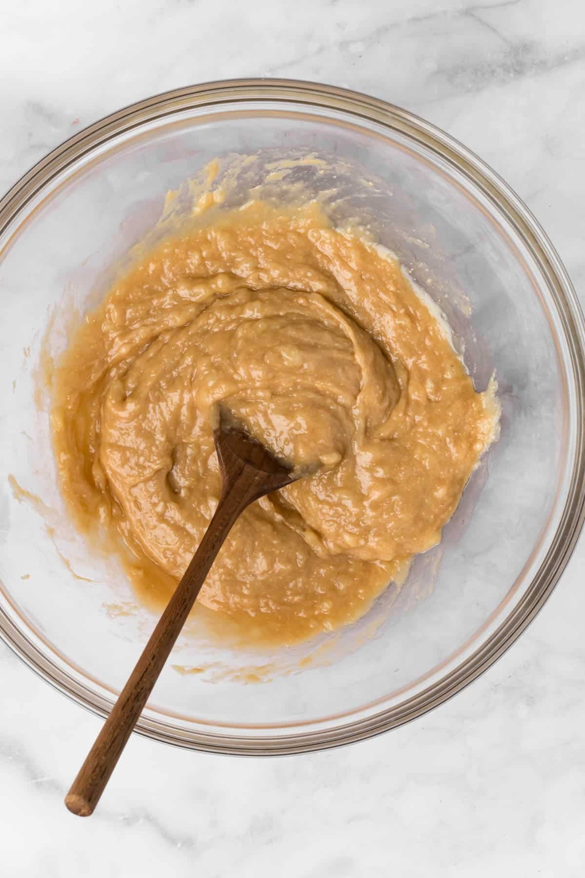Overhead view of a wooden spoon stirring the wet ingredients for breakfast cookies and a glass bowl.