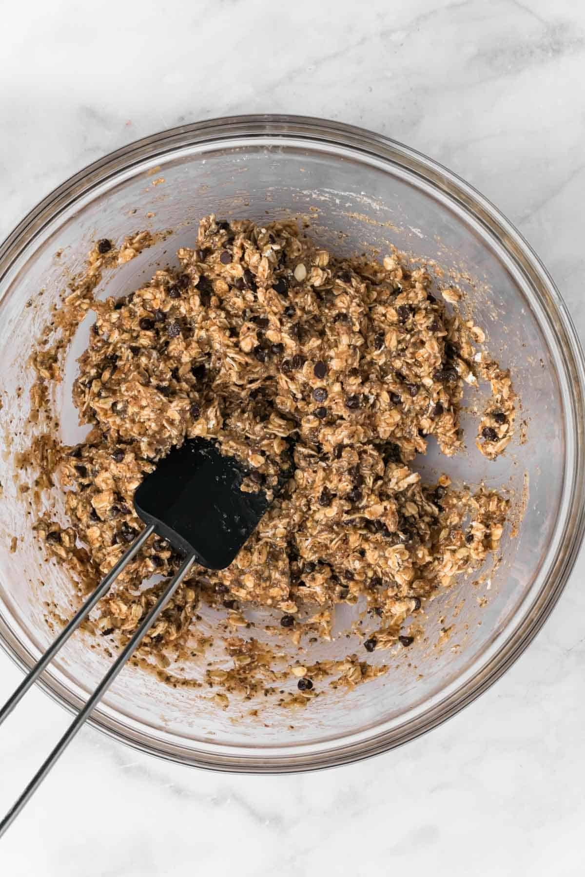 Overhead view of a black spatula mixing breakfast cookie dough in a glass bowl.