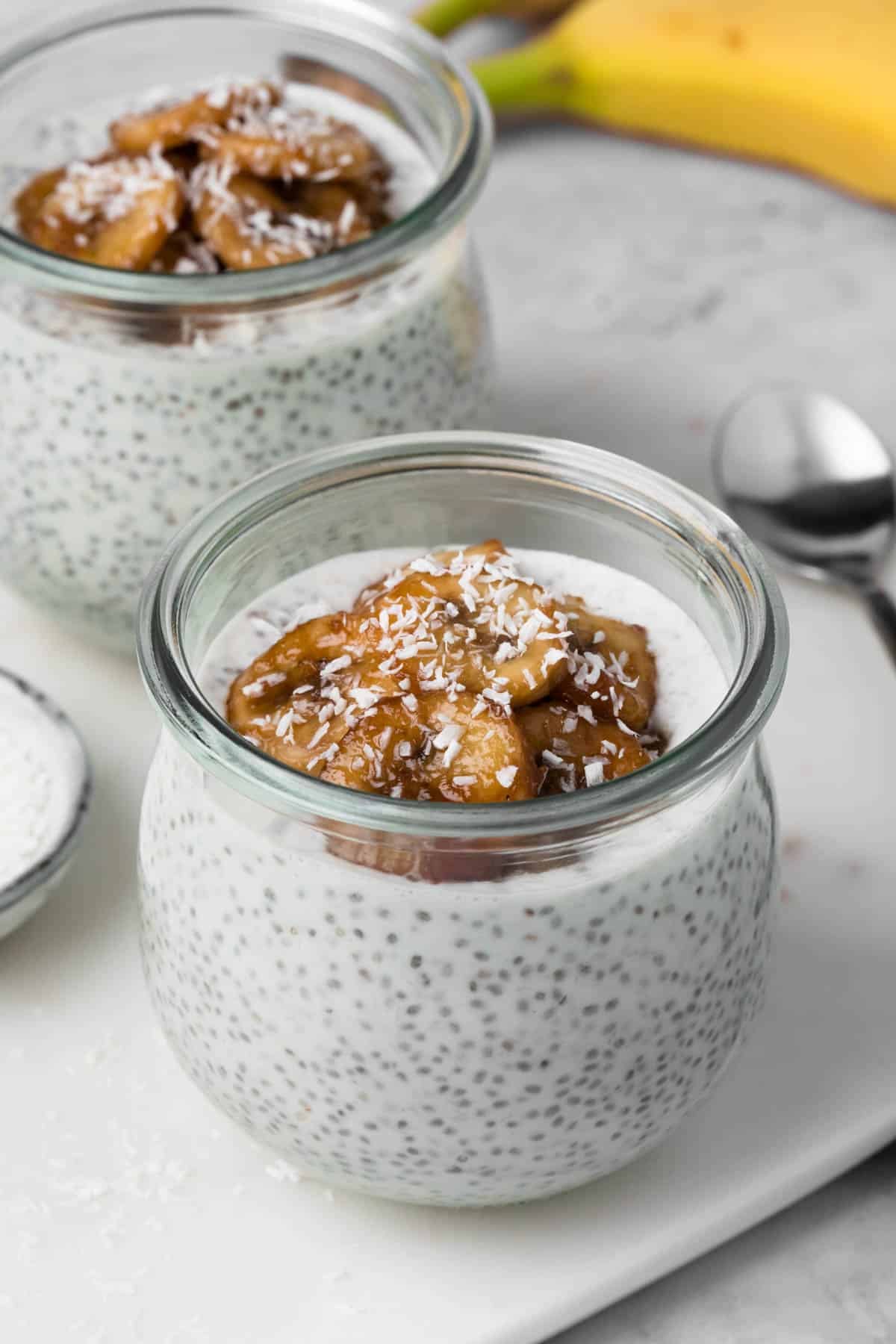 Side view of coconut chia pudding topped with caramelized bananas in 2 glass jars.