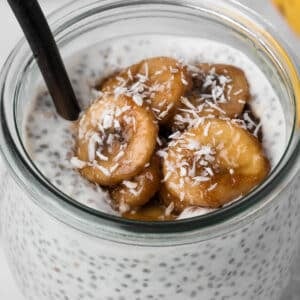 Side view of coconut chia pudding topped with caramelized bananas in a glass jar.