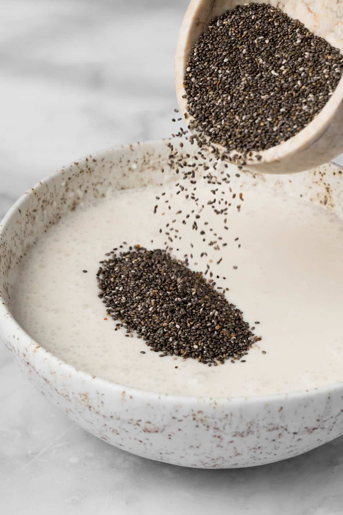 Side view of chia seeds being poured into a bowl of coconut milk.